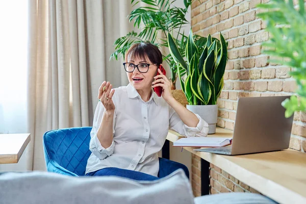 Kobieta Średnim Wieku Rozmawiająca Przez Telefon Komórkowy Siedząca Biurkiem Domu — Zdjęcie stockowe
