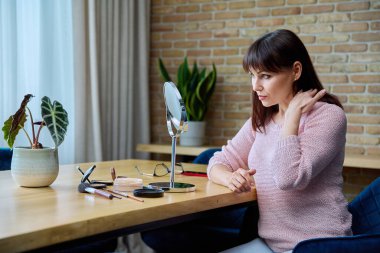 Mutlu, orta yaşlı, güzel bir kadın. Yüzüne dokunuyor, aynada kendine hayran. Olgun kadın, estetik cerrahi kolajen enjeksiyonlarının sonucu olan cilt durumundan memnun. Profesyonel bakım, güzellik.