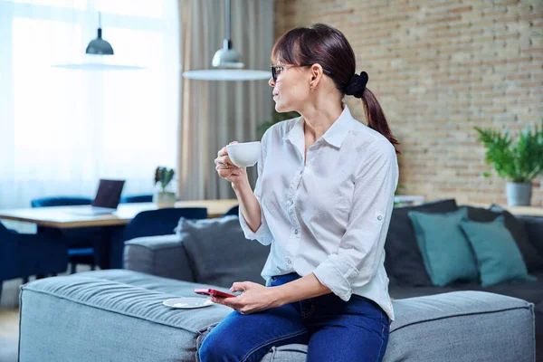 Kobieta Średnim Wieku Używa Smartfona Pije Kawę Domu Kanapie Dojrzałe — Zdjęcie stockowe