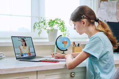 İnternette video dersi alan küçük bir kız, evdeki masasında oturuyor, dizüstü bilgisayar kullanıyor. Teknoloji, bilgi, eğitim, e-öğrenme, uzak online dersler, özel ders, lise konsepti