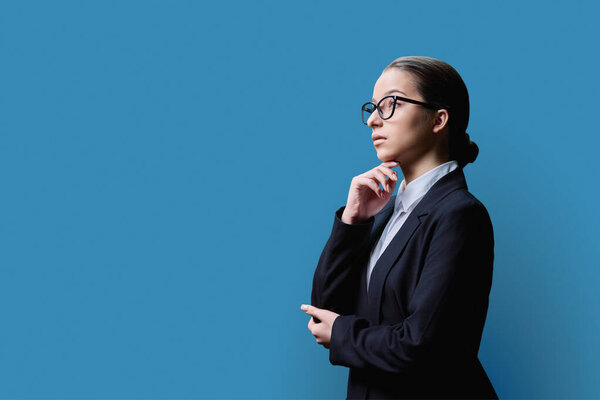 Profile view, portrait of serious young teenage student female in black jacket on blue studio background, girl looking at empty space for your advertisement information text, copy space