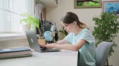 Ergen bir kız, evinde, masasında laptopunda daktilo yazıyor. Lise, gençlik, eğitim, teknoloji, bilgi kavramı