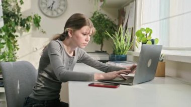 Ergen bir kız, evinde, masasında laptopunda daktilo yazıyor. Lise, gençlik, eğitim, teknoloji, bilgi kavramı