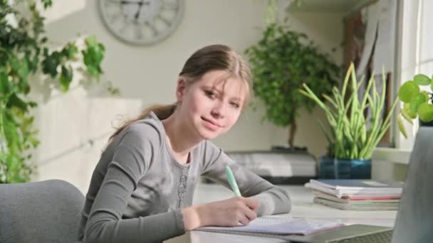 照片上的少女坐在家里书桌前 带着手提电脑 笑着看着12 13岁的女学生看着相机 青春期 生活方式概念 — 图库视频影像
