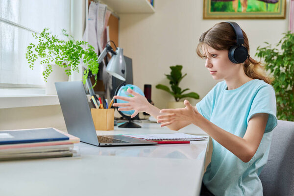 Preteen girl in headphones having video lesson on laptop, at desk at home. Online learning, tutoring, learning webinars, e-learning education technology concept