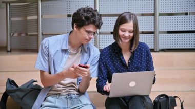 Arkadaşları üniversite öğrencisi erkek ve kız eğitim binasının içinde akıllı telefon dizüstü bilgisayarı var. Gençlik, yaşam tarzı, teknoloji, eğlence iletişimi için mobil uygulamalar