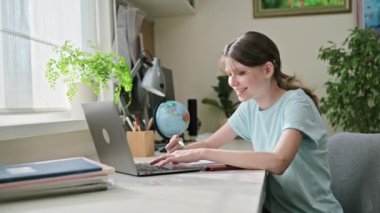 Genç liseli kız, dizüstü bilgisayarla evde ders çalışıyor. Video dersi sohbeti yapıyor. Webinar 'ı dikkatle dinleyip not alıyor. Teknoloji eğitimi gençliği