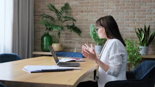 成熟したビジネス女性は コンピュータを使用してオフィスの机に座ってビデオ会議を持っています ラップトップ画面 ビデオチャットコールを見ている肯定的な話す女性 リモートミーティング オンライン相談 — ストック動画