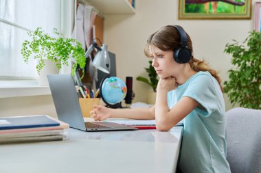 Kulaklık takan, dizüstü bilgisayarda video dersi alan, evdeki masada oturan bir kız. Çevrimiçi öğrenim, öğretim, öğrenme webinarları, e-öğrenme eğitim teknolojisi konsepti