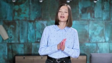 Mavi gömlekli genç bayan kameraya bakıyor, kadın kayıt blogu, vlog, webinar, evde oturma odasının arka planında. Modern teknoloji, yayın, gençlik, serbest çalışma konsepti