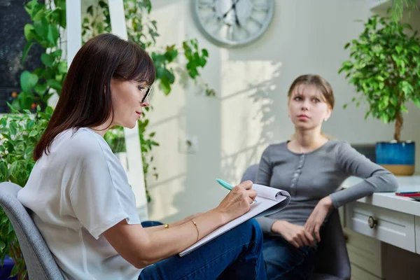 Sad teenage girl at therapy meeting with psychologist, counselor. An upset girl, high school student, sitting in mental specialists office. Child psychology, psychotherapy, social life of teenager