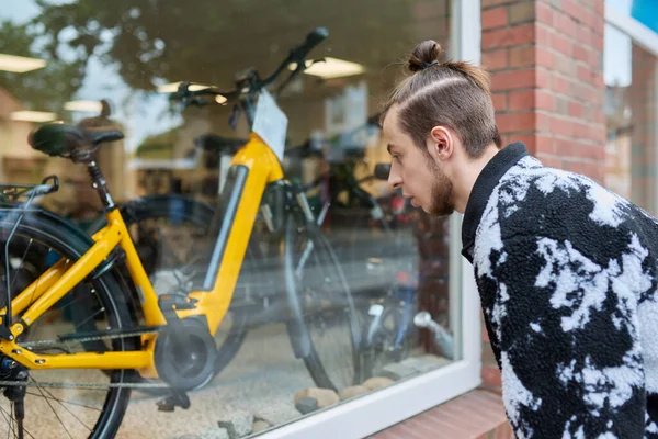 Young male looking dreamily at modern bicycles in shop window. Sale purchase of bicycles, small business, active lifestyle, urban transport concept