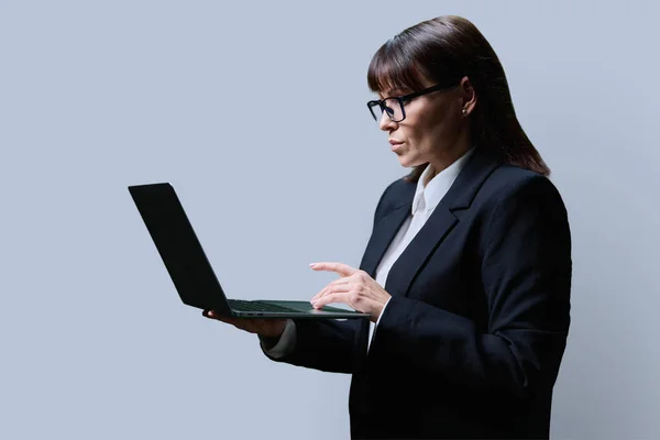Серйозна Зріла Жінка Використовуючи Ноутбук Руках Сірому Фоні Студії Діловий — стокове фото