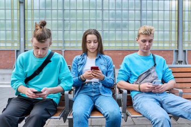 Bir grup genç arkadaş tren istasyonundaki sandalyelerde oturan akıllı telefonları kullanıyor. Gençlik, ergenlik, dijital teknoloji, mobil uygulamalar, iletişim eğlence öğrenme sosyal ağları