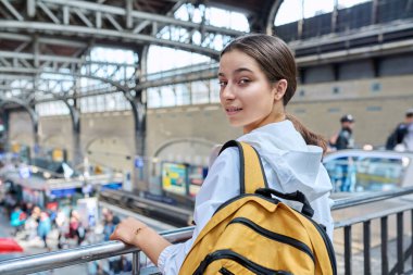 Sırt çantalı genç kız tren istasyonunda kameraya bakıyor. Lise öğrencisi, genç kız yolcu, banliyö ve şehirlerarası tren ulaşımı