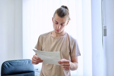 Ciddi bir genç erkek öğrenci. 19-20 yaşlarında. Evde önemli bir mektup okuyor..