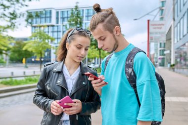 Genç arkadaşlar, ellerinde akıllı telefonlar, şehrin dışında cep telefonlarını kullanarak ekranlara bakıyorlar. Boş zaman çalışması iletişimi için internet dijital teknoloji uygulamaları