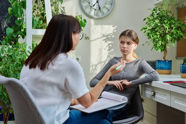 Sad teenage girl at therapy meeting with psychologist, counselor. An upset girl, high school student, sitting in mental specialists office. Child psychology, psychotherapy, social life of teenager