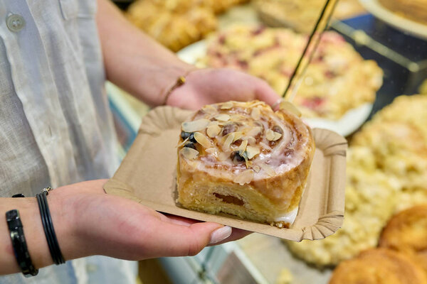 Bun with marzipan in hands, against the backdrop of display case in pastry bakery. Delicious fresh pastries, flour food, bakery cafeteria small business concept