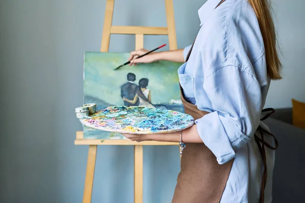 マルチカラーのアクリル塗料を施したパレットのクローズアップ キャンバスにイーゼル絵を施したブラシ付きの女性アーティストの手 創造性 アートセラピーのコンセプト — ストック写真