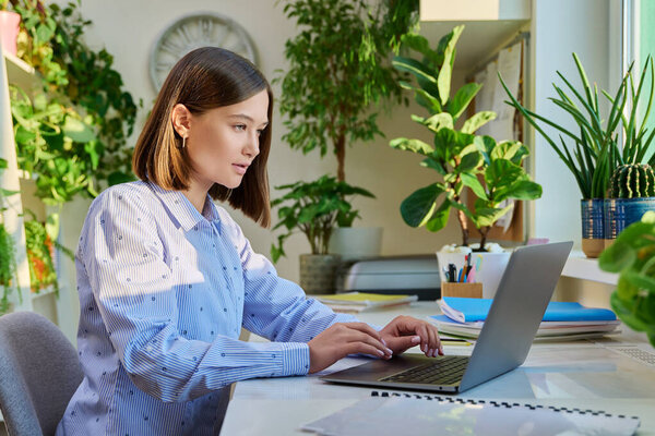 Young woman typing on laptop computer at home. Female freelancer, an employee working remotely, university student studying online preparing for exams. Technology youth training education work concept