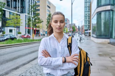 Genç lise öğrencisinin portresi. 16-17 yaşlarında, sırt çantalı, modern şehrin sokaklarında kameraya bakan kendine güvenen bir kız. Şehir hayatı, ergenlik, eğitim, gençlik kavramı