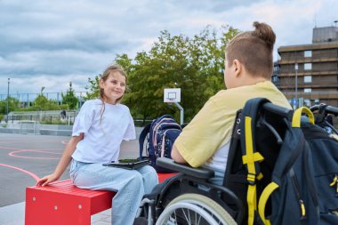 Tekerlekli sandalyedeki erkek ve kız çocuklarının arkadaşlık iletişimi. Sınıf arkadaşları okuldan sonra oturup konuşuyorlar. Eğitim, engellilik, kapsayıcılık kavramı