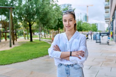 Modern şehrin caddesinde çapraz kollarıyla kameraya bakan kendine güvenen genç kızın portresi. Ergenlik, kentsel yaşam tarzı, gençlik kavramı