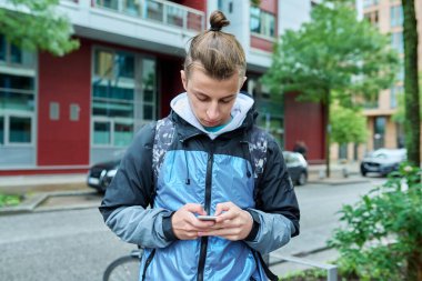 Şehirde akıllı telefon kullanan, sırt çantalı, şık, genç bir erkek. Moda saç stili sakallı hippi elinde telefonla turizm seyahati iletişim eğlence çalışması için mobil uygulamalar yapıyor.