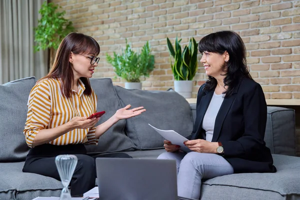 stock image Two mature business women having conversation sitting on couch in office, discussing work, commercial projects. Communicating female colleague, 40s 50s age. Law finance mentoring consulting teamwork