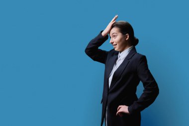 Görüntü metniniz için profil oluşturan neşeli genç bayan, mavi stüdyo arka planı. Şok olmuş genç kız öğrenci resmi giyinmiş, gençlik eğitimi almış.