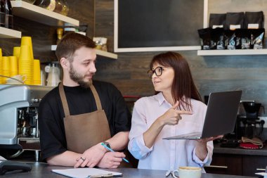 Takım, ortaklar, genç erkek ve olgun kadın, kafede barda dizüstü bilgisayar kullanarak konuşuyorlar. Takım, küçük işletme, iş, personel, kafeterya restoranı, girişimcilik konsepti