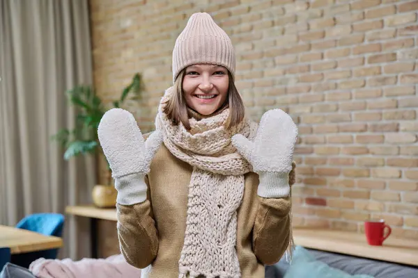 年轻迷人而快乐的女人穿着舒适温暖的衣服 头戴针织羊毛衫帽巾 在客厅里看着相机 寒冬秋冬 人的观念 — 图库照片