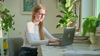 Evde dizüstü bilgisayarda yazan gülümseyen genç kız. Kadın serbest çalışan, uzaktan çalışan bir çalışan, internetten sınavlara hazırlanan bir üniversite öğrencisi. Teknoloji gençlik eğitimi çalışmaları