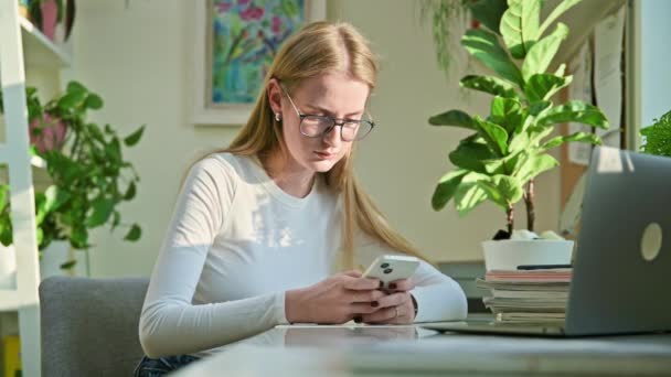 若い10代の女性大学生がスマートフォンでテキストを入力し 友人とチャットし 机の部屋で自宅に座っている モバイルアプリケーション ソーシャルネットワーク オンラインコミュニケーション — ストック動画
