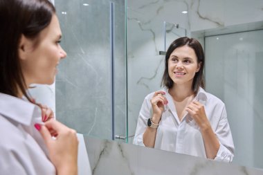 Banyodaki aynada yüzüne bakan genç bir kadın. 30 yaş, güzellik, doğal makyaj, saç bakımı konsepti