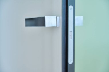 Krom, modern bir kapı kolunun beyaz, parlak bir kapıya yakın çekimi. Modern minimalizm tarzı, kapı mobilyası, iç mekan ayrıntıları