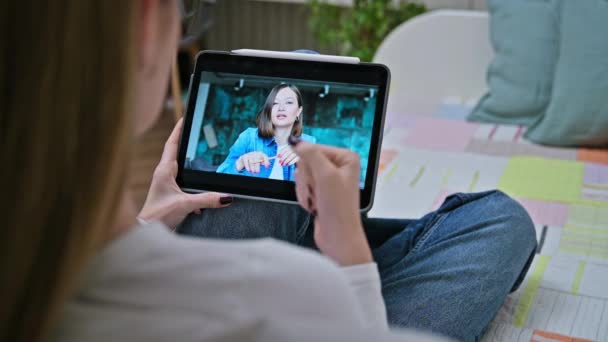 教育的なオンラインウェビナーを聞く若い女性は 家庭でソファーに座って デジタルタブレットを使用して スクリーン上の講師と リモートレッスン 若者のコンセプト — ストック動画