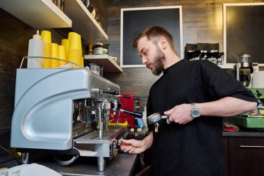 Kahve dükkanında kahve hazırlayan erkek barmen, kahve makinesinin yanında duran önlüklü, sakallı genç adam. Küçük işletme, yemek servisi işi, kahve dükkanı, personel, iş konsepti