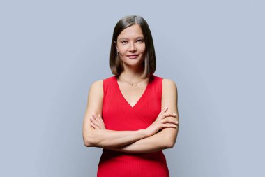 Gri stüdyo arka planında kendine güveni tam genç bir kadının portresi. Kollarını kavuşturup kameraya bakan başarılı, modaya uygun bir kadın. İş, iş, hizmet, eğitim, moda güzellik meslekleri