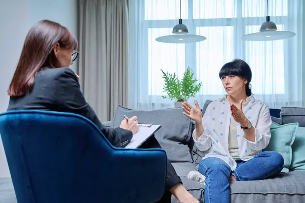 Mature 50s woman having therapy session with psychologist sitting on sofa in office. Mental health of senior people, counseling, treatment, psychological help support, psychology psychotherapy concept