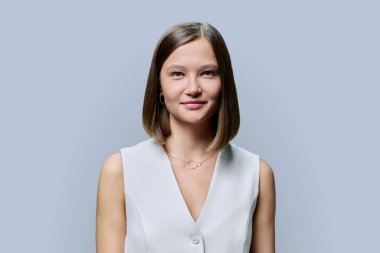 Gri stüdyo arka planında zarif bir iş kadınının portresi. Beyaz yelekli, doğal makyajlı, gülümseyen kadın kameraya bakıyor. Güzellik, moda, bakım, kozmetik, yüz kılları
