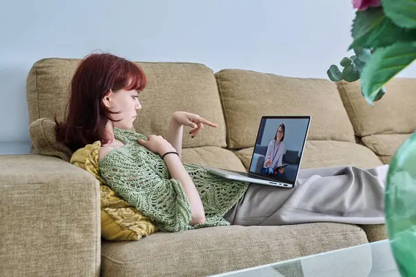Online therapy, young teenage female lying at home in living room on sofa having video conference call with professional psychologist. Psychology, psychotherapy, counseling, mental health of youth
