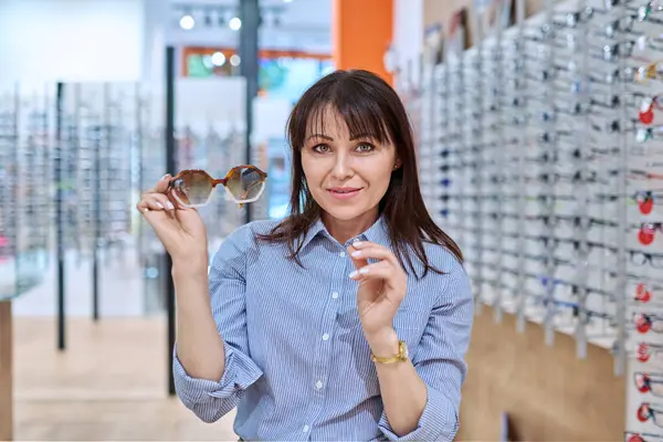 Middle-aged woman in an optical store choosing to buy sunglasses. Fashion, accessories, eye health