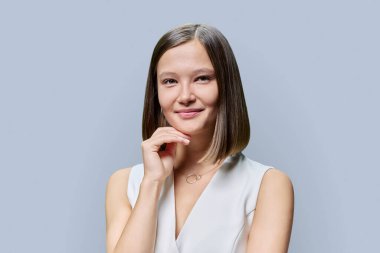 Moda makyajlı, dudakları kirpikli, gri stüdyo arka planında saç stili olan çekici genç bir kadının güzel portresi. Sağlıklı saç, sağlıklı cilt, bakım, kozmetik konsepti