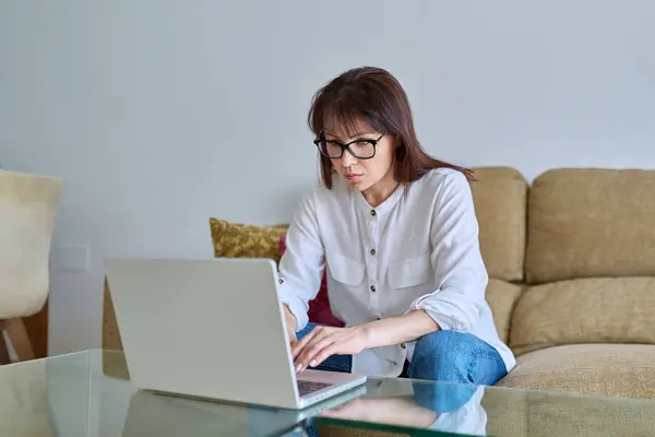 ラップトップコンピュータで働く真剣な中年女性 自宅のオフィスの机に座って — ストック写真