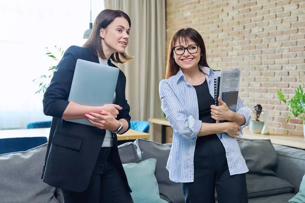 Two business women colleagues talking together in office. Young and middle-aged females, teachers psychologists accountants, work business education, staff professions, teamwork office workers concept