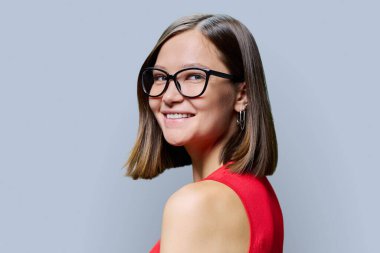 Moda gözlüklü gülümseyen genç bir kadının vesikalık portresi, yüzü gri stüdyo arka planında. Moda, tarz, gözlük satışı, optik mağazası, insan sağlığı güzellik konsepti