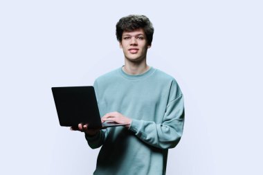 Laptop kullanan genç bir üniversite öğrencisi, beyaz stüdyo geçmişi var. Kameraya bakan gülümseyen yakışıklı adam. İnternet teknolojileri, çevrimiçi öğrenim istirahatı, sanal uzaktan eğitim eğlence iletişimi