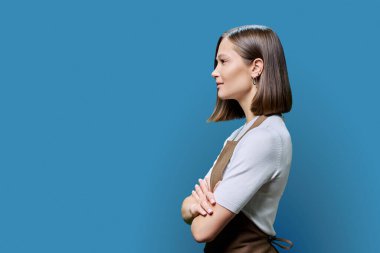 Profil görüntüsü, önlüklü başarılı, başarılı, kolları çapraz çalışan genç kadın çalışanı, mavi kopya stüdyo arka planı, reklam metni için alan. İş, iş, iş, hizmet, insan